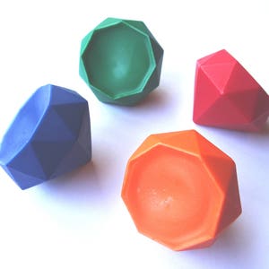 May include: Four colorful, geometric-shaped objects resembling gemstones. The objects are in shades of blue, green, red, and orange. The objects are arranged on a white surface.