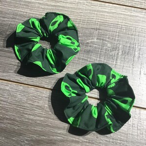 May include: Two green and black hair scrunchies with a repeating alien pattern.