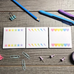 May include: Three rainbow-colored sticky note pads with different designs. The first pad has a row of stars, the second has a row of lightning bolts, and the third has a row of hearts.
