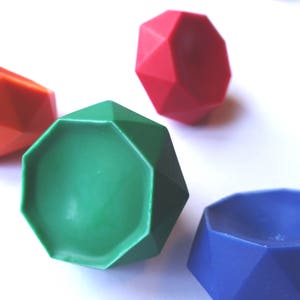May include: An assortment of colorful, geometric-shaped objects in red, green, orange, and blue. The objects have a faceted design, resembling gemstones or decorative pieces. The image is set against a white background.