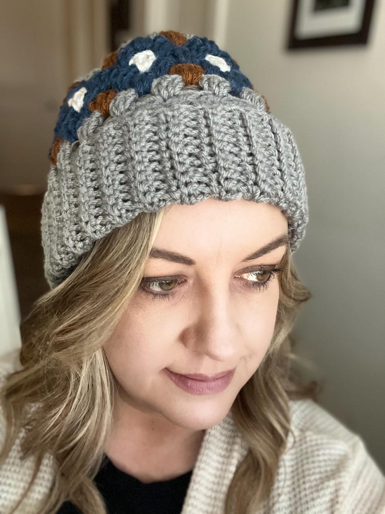 May include: A grey crocheted beanie with a colourful geometric pattern on the top. The pattern features brown, blue, white and cream squares.