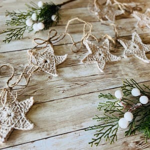 May include: A garland of crocheted burlap stars strung together with twine. The garland is decorated with white berries and greenery.