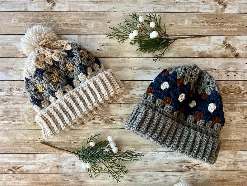 May include: Two crocheted hats with different colour patterns. One hat is beige with brown and yellow accents, and the other is grey with brown, blue, and white accents.