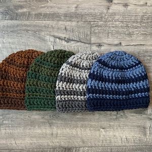 May include: Four crocheted beanies in different color combinations. The beanies are brown and orange, green and brown, gray and white, and blue and black.