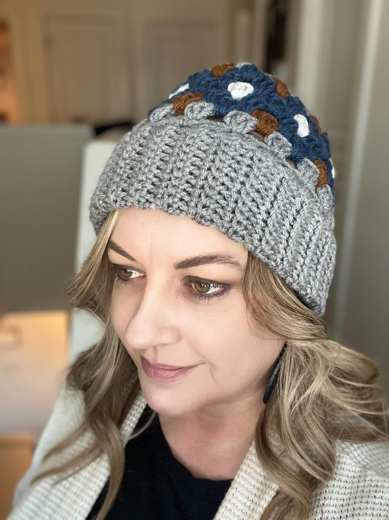 May include: A grey crocheted beanie with a colourful geometric pattern on the top. The pattern features squares of blue, brown, white, and grey yarn.