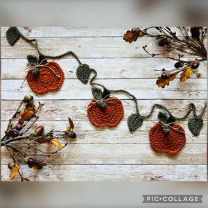 May include: A crochet garland featuring three orange pumpkins with dark green leaves connected by a vine. Each pumpkin is accented with a small piece of twine tied around the stem. The garland is displayed alongside branches with acorns.