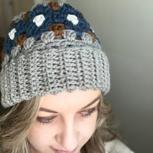 May include: A grey crocheted beanie with a brown, white and blue geometric pattern on the top.