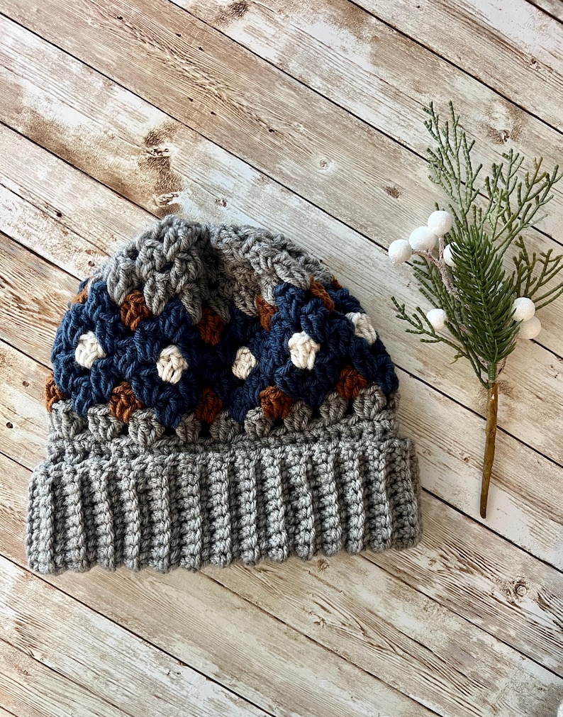 May include: A grey and blue crocheted beanie with a brown and white pattern. The beanie has a ribbed brim.