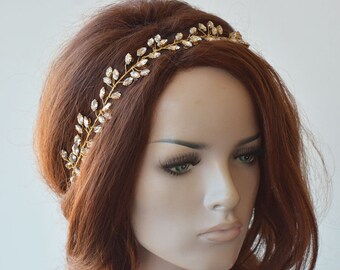May include: A gold headband with clear crystal embellishments in a leaf design. The headband is worn by a mannequin with long, red hair.