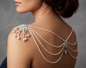 May include: A pearl and crystal shoulder piece. The design features a central cluster of crystals with pearl drops, and multiple strands of pearls that drape across the back. A sophisticated accessory for weddings or special events.