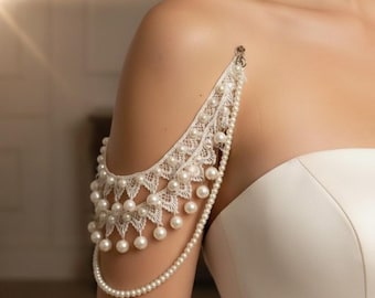 May include: A delicate, white lace shoulder piece adorned with numerous small, round pearls. The design features a scalloped edge and a cascade of pearls, creating an elegant, feminine accessory. The shoulder piece is attached with a small clasp.