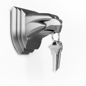 May include: A silver metal key holder shaped like a stylized hand with a set of keys hanging from it.