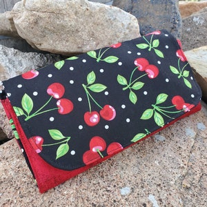 May include: A black fabric wallet with a red lining and a cherry print. The cherries are red with green stems and leaves. The fabric has white polka dots.