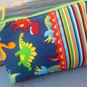 May include: A blue zippered pouch with a colourful striped fabric on one side and a dinosaur print on the other side. The dinosaur print features green, yellow, red, and orange dinosaurs on a dark blue background.