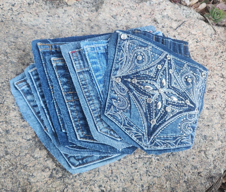 Pu&ograve; includere: Una pila di sottobicchieri in denim, ciascuno realizzato con tasche di jeans riciclate. I sottobicchieri variano nelle tonalit&agrave; di blu, uno dei quali presenta un design a stella ricamato impreziosito da strass. Un articolo di arredamento per la casa sostenibile.