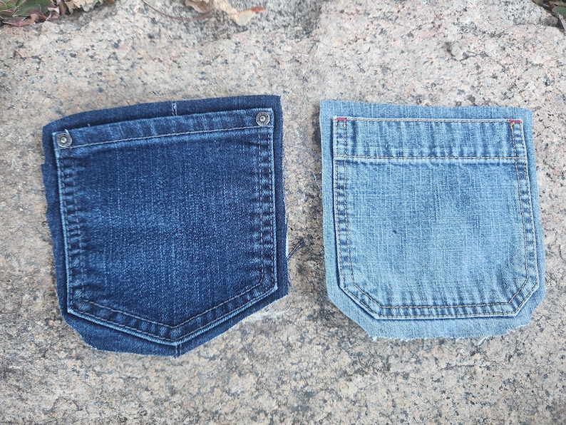 Pu&ograve; includere: Due tasche di jeans in denim. Una &egrave; di un lavaggio blu scuro, l'altra &egrave; di un lavaggio blu chiaro. Entrambe le tasche hanno una forma rettangolare con il fondo curvo e sono cucite con un filo a contrasto. La tasca blu scuro ha un bottone argentato.