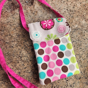 May include: A small pink and white crossbody bag with a polka dot pattern and floral design. The bag has a pink strap and a flap closure.