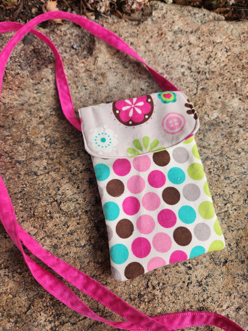 May include: A small pink and white crossbody bag with a polka dot pattern and floral design. The bag has a pink strap and a flap closure.