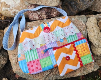 May include: A colorful patchwork fabric purse with a blue strap and a smaller matching zippered pouch. The purse has a white lace trim and red buttons.