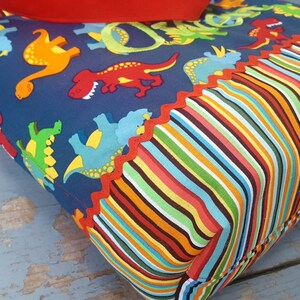 May include: A blue tote bag with a dinosaur print and a colourful striped bottom. The bag has a red scalloped trim.