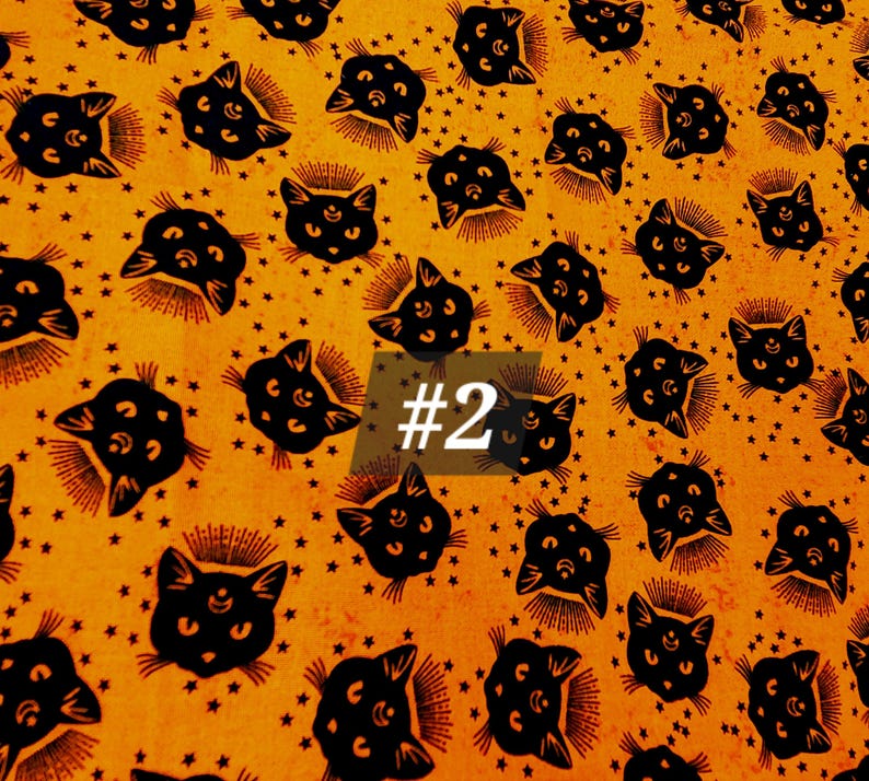 May include: Orange fabric with a repeating pattern of black cats with three eyes and a crescent moon. The cats are surrounded by small stars. The text '#2' is visible in the centre of the image.