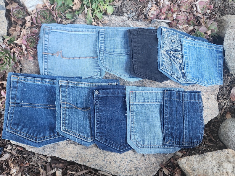 Pu&ograve; includere: Una collezione di tasche di jeans in varie tonalit&agrave; di blu e nero, disposte su una superficie di pietra. Le tasche presentano diversi modelli di cucitura e stili, mostrando la variet&agrave; di trame e lavaggi del denim.