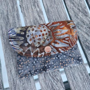 May include: A small, brown and gray fabric wallet with a snap closure. The wallet has a floral pattern on the front and a polka dot pattern on the back.