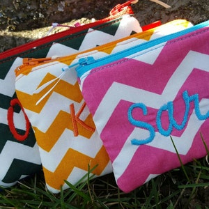 May include: Five small zippered pouches with chevron patterns in different colors. The pouches are personalized with the letters A, O, K, and the name Sarah.
