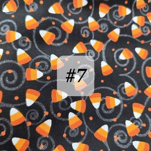 May include: Black fabric with a repeating pattern of orange and white candy corn, small orange dots, and white swirls. The number "#7" is written in white on a white square.