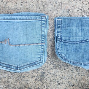 Pu&ograve; includere: Due tasche di jeans in denim blu chiaro. Una tasca ha un design decorativo con cuciture marroni. L'altra tasca ha una forma arrotondata con una cucitura curva. Entrambe le tasche sono su una superficie grigia strutturata.