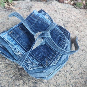 Pu&ograve; includere: Una pila di sottobicchieri in denim in varie tonalit&agrave; di blu, legati con un cinturino in denim abbinato. I sottobicchieri sono realizzati in denim riciclato e presentano dettagli di tasche visibili.