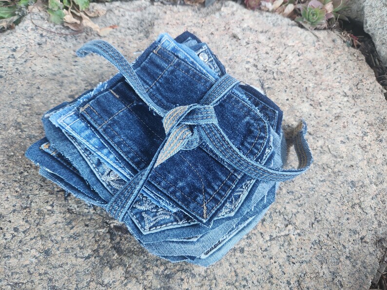 Pu&ograve; includere: Una pila di sottobicchieri in denim in varie tonalit&agrave; di blu, legati con un cinturino in denim abbinato. I sottobicchieri sono realizzati in denim riciclato e presentano dettagli di tasche visibili.
