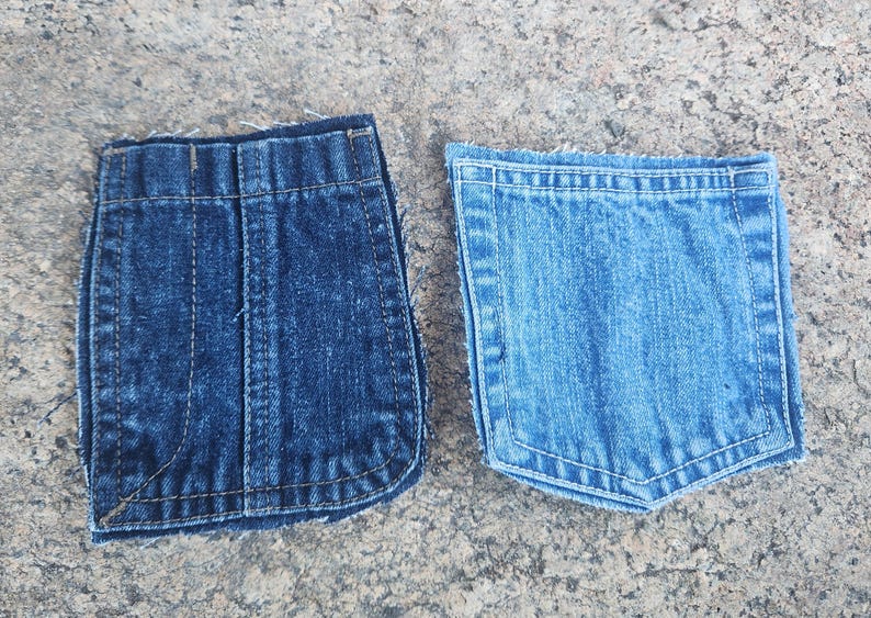 Pu&ograve; includere: Due tasche di jeans in denim, una blu pi&ugrave; scuro e l'altra blu pi&ugrave; chiaro, sono esposte fianco a fianco. Entrambe le tasche hanno cuciture visibili e sono appoggiate su una superficie grigia strutturata.