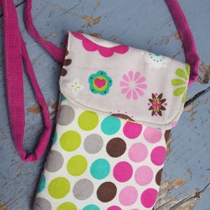May include: A small pink and white fabric phone case with a polka dot pattern and floral design. The case has a pink strap.