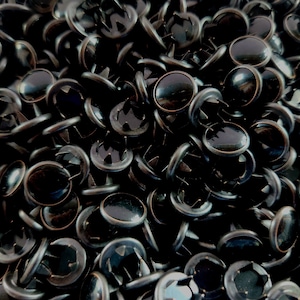 May include: A close-up image of a pile of black metal rivets with a shiny finish. The rivets have a round head and a pointed base.