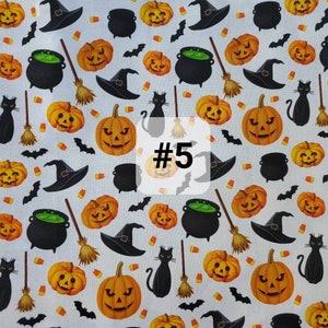 May include: A white fabric with a repeating pattern of black cats, witches' hats, pumpkins, cauldrons, bats, and broomsticks. The fabric has the number "#5" printed on it.