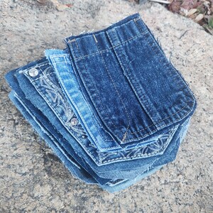 Pu&ograve; includere: Una pila di tasche in denim in varie tonalit&agrave; di blu. Alcune tasche hanno cuciture decorative e dettagli di strass. Le tasche sono disposte su una superficie grigia strutturata.