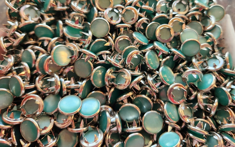 Puede incluir: Un mont&oacute;n grande de tachuelas met&aacute;licas redondas de color turquesa con acabado plateado. Las tachuelas tienen una parte superior redondeada elevada y una base puntiaguda.