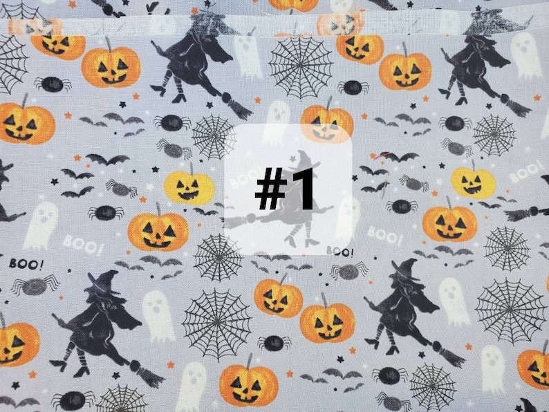May include: A grey fabric with a Halloween theme featuring black witches, orange pumpkins, spiders, bats, and the words "Boo!" and "#1".