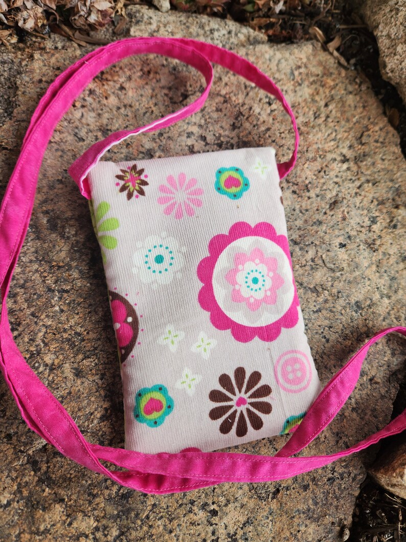 May include: A small pink crossbody bag with a floral print. The bag has a pink strap and a white background with pink, green, brown, and blue flowers.