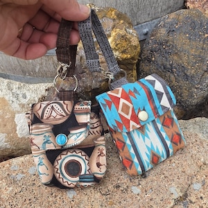May include: Two small fabric pouches with wrist straps and metal snap closures. One pouch features a black background with tan and blue pottery motifs, while the other displays a geometric pattern in shades of blue, orange, and white.