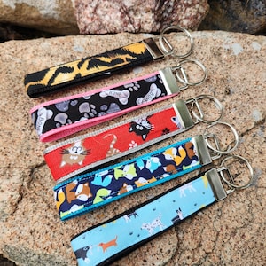 May include: Six colorful keychains with different animal prints and designs. The keychains feature a variety of animals, including cats, dogs, and paw prints. The keychains are attached to silver key rings.