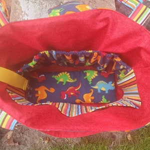 May include: Red tote bag with a yellow strap and a blue and white dinosaur print lining. The bag has a striped fabric trim.