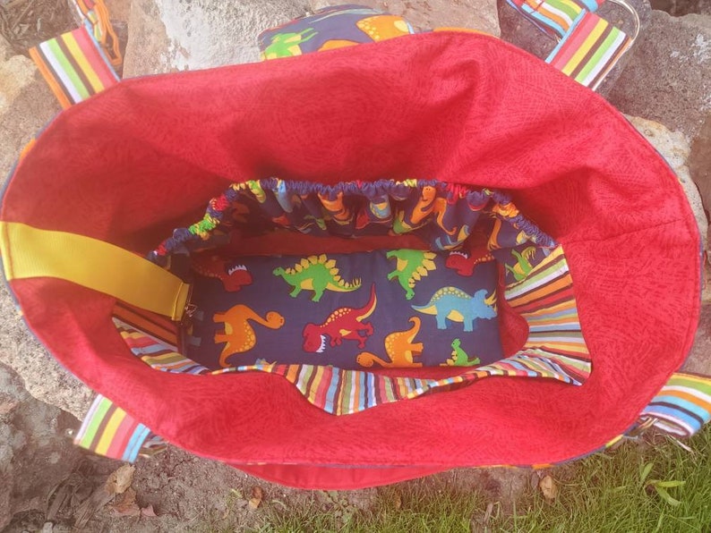 May include: Red tote bag with a yellow strap and a blue and white dinosaur print lining. The bag has a striped fabric trim.