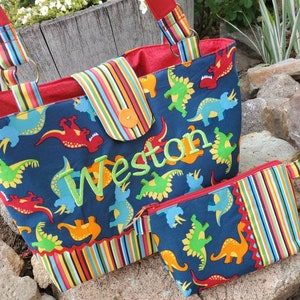 May include: A blue and red tote bag with a colourful striped trim and a dinosaur print. The bag has a zipped pocket and is personalised with the name "Weston".