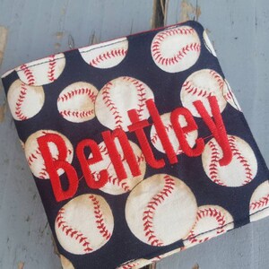 May include: A black fabric wallet with a baseball pattern and the name "Bentley" embroidered in red.