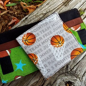 May include: Two fabric wallets with a basketball theme. One wallet is green with a blue star and the other is gray with white text that says "POINTER FREE JUMP INNER FREE GUARD PASZKEE TEAM D 3 POINTER".