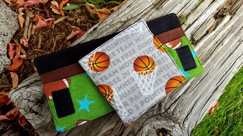 May include: Two fabric wallets with a basketball theme. One wallet is green with a blue star and the other is gray with white text that says "POINTER FREE JUMP INNER FREE GUARD PASZKEE TEAM D 3 POINTER".