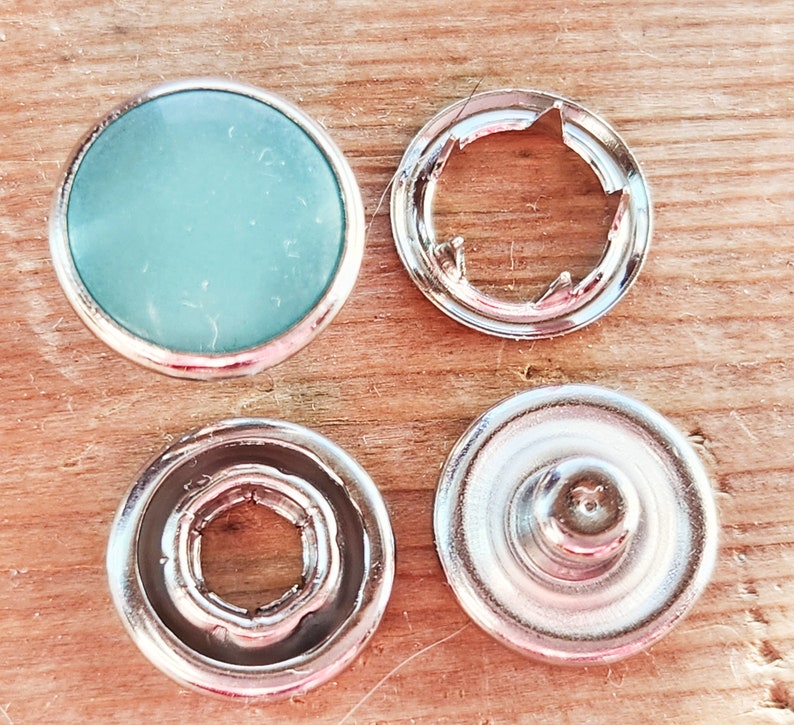 Puede incluir: Cuatro botones a presi&oacute;n plateados, uno con un centro azul claro y tres con un dise&ntilde;o circular.