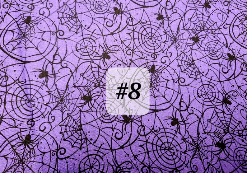 May include: Purple fabric with a black spiderweb and spider pattern. The fabric has the number 8 printed on it.